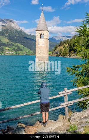 Un sportif habillé observe le célèbre clocher submergé du lac Resia à Curon (Graun), dans le Tyrol du Sud, en Italie Banque D'Images