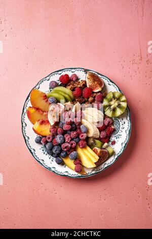 Assortiment de fruits en tranches sur une assiette vintage. Vue de dessus de la mangue, des kiwis, des figues, du raisin, des bananes, des framboises et des bleuets sur fond rose. Banque D'Images