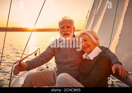 Portrait d'un beau et heureux couple senior amoureux enferme et profite d'un coucher de soleil extraordinaire tout en étant assis sur le côté de voilier ou de pont de yacht Banque D'Images