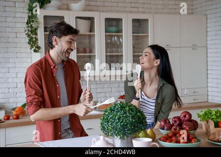 Heureux beau couple préparant des aliments sains dans la cuisine moderne à la maison, rire et s'amuser, en appréciant le temps libre ensemble Banque D'Images