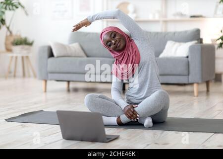 Home Training. Femme musulmane noire dans hijab pratiquant des sports en ligne avec un ordinateur portable Banque D'Images