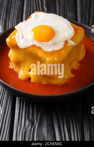 Sandwich Francesinha portugais chaud avec différents types de saucisses et de viande, versé avec une sauce à la bière de tomate et recouvert d'un œuf frit en gros plan Banque D'Images