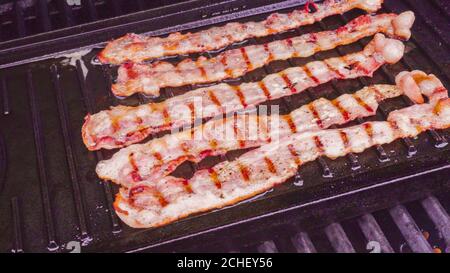 Cuisson de tranches de bacon sur un barbecue à gaz extérieur. Banque D'Images