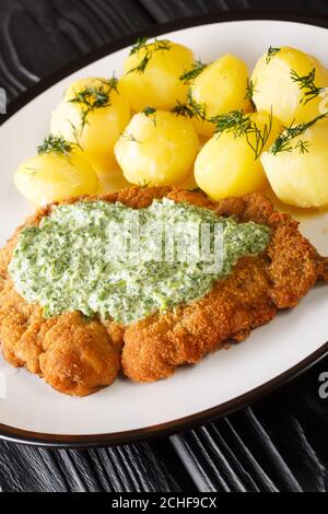 Schnitzel allemand aux pommes de terre bouillies et sauce verte de Francfort en gros plan dans une assiette sur la table. Verticale Banque D'Images