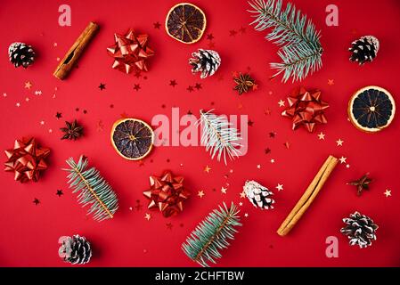Composition de Noël. Branches de sapin, cônes de pin, fruits secs et confettis festifs sur fond rouge, vue du dessus Banque D'Images