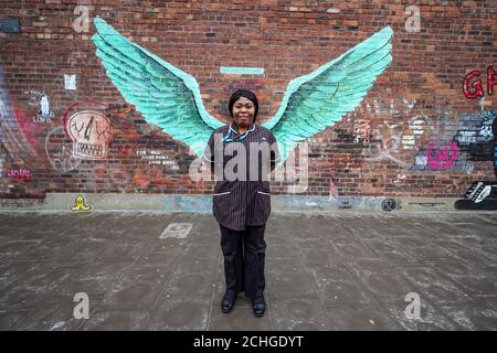 Susan Tay, matronne communautaire au Mersey Care NHS, se dresse devant les « Liver Bird Wings », une œuvre de Paul Curtis sur un mur dans le triangle Baltique de Liverpool. Banque D'Images