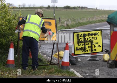 Un travailleur retire un spray à la hâte peint sur un panneau à l'entrée d'une route fermée et d'un parking près du phare de Whitley Bay, Northumberland. Graffiti a été affiché sur des panneaux dans plusieurs parkings le long de la route côtière de Northumberland alors que le Royaume-Uni continue à se verrouiller pour aider à freiner la propagation du coronavirus. Banque D'Images