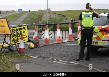 Une voiture de police bloque la route où une croix de croix a été peinte sur un panneau à l'entrée d'une route fermée et d'un parking près du phare de Whitley Bay, Northumberland. Graffiti a été affiché sur des panneaux dans plusieurs parkings le long de la route côtière de Northumberland alors que le Royaume-Uni continue à se verrouiller pour aider à freiner la propagation du coronavirus. Banque D'Images