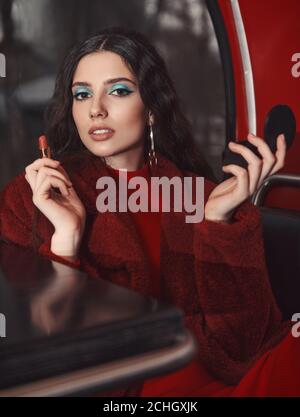 Jolie fille assise dans le café-bus (bistro) avec rouge à lèvres et miroir. Portrait rétro (vintage) d'une belle jeune femme élégante au restaurant, portant Banque D'Images