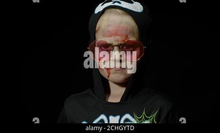 Halloween horreur, fille en colère avec le maquillage de sang sur son visage. Enfant habillé comme squelette effrayant avec des lunettes de soleil, posant, faisant des visages sur fond noir. Concept du vendredi 13 Banque D'Images