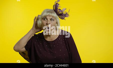 Portrait d'une vieille femme âgée qui entend parler en privé, qui tente de trouver des secrets personnels, qui espionne. Vieille dame élégante grand-mère sur fond jaune dans le studio Banque D'Images