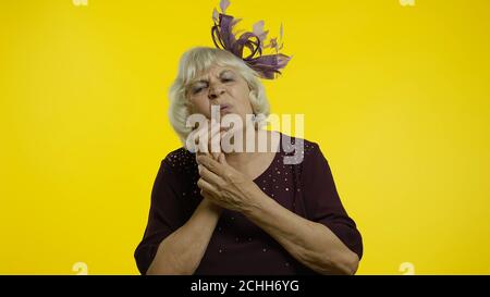 Problèmes dentaires. Une vieille femme âgée frustrée touchant une joue douloureuse, contrariée par un mal de dents terrible, une douleur horrible causée par des cavités et une maladie des gencives. Grand-mère de style âgé sur fond jaune Banque D'Images