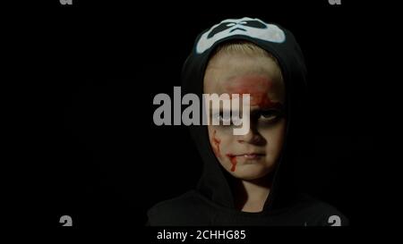 Halloween, fille en colère avec le maquillage de sang sur son visage. Enfant habillé comme squelette effrayant, posant, faisant des visages agressifs sur fond noir. Concept de l'horreur des fêtes. Thème du vendredi 13 Banque D'Images