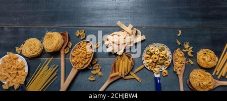 Concept de cuisson des pâtes. Pâtes crues différentes formes et cuillères sur fond de table en bois bleu, vue du dessus Banque D'Images