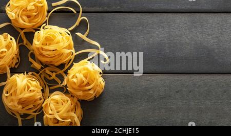 Concept de cuisson des pâtes. Tagliatelle de pâtes crues nichent sur fond de table en bois bleu, vue du dessus, espace de copie Banque D'Images