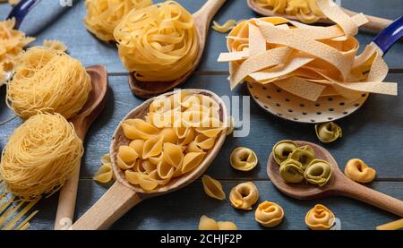 Concept de cuisson des pâtes. Pâtes crues différentes formes et cuillères plat sur fond de table en bois bleu, vue rapprochée Banque D'Images