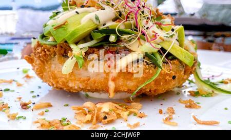 Les hybrides sushi-alimentation tendance. Nouveau design délicieux ingrédients de hamburger au riz blanc saumon, avocat, mayonnaise, légumes frais, oignon frit. Arrière-plan de mise au point douce Banque D'Images