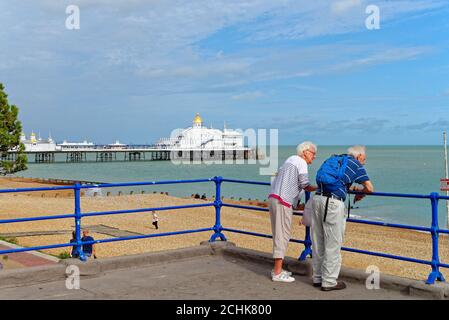 Un couple âgé regardant la vue depuis le front de mer d'Eastbourne avec la jetée en arrière-plan, un soir d'été, East Sussex Angleterre Royaume-Uni Banque D'Images