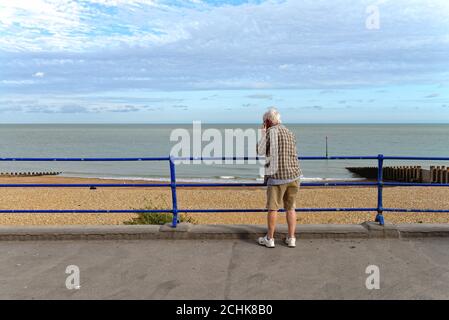 Vue arrière d'un homme âgé utilisant un téléphone portable sur le front de mer d'Eastbourne avec la mer en arrière-plan, East Sussex Angleterre Banque D'Images