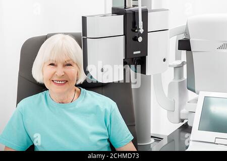 Vérifier la vue de la femme âgée souriante sur le phoropter moderne. Si une femme a une mauvaise vue, le médecin donnera une ordonnance pour des lunettes Banque D'Images