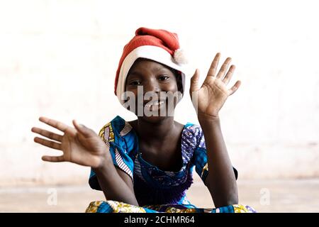 Magnifique écolière africaine posant pour Noël avec chapeau et mains Ouvrir Banque D'Images