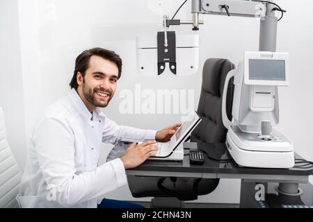 Optométriste souriant assis sur son lieu de travail dans une clinique moderne. Examen oculaire et diagnostic de la vision Banque D'Images