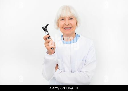 Portrait d'une femme ORL médecin expérimentée aux cheveux gris dans un otoscope dans ses mains sur fond blanc Banque D'Images