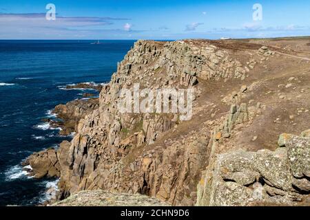 Vue sur la falaise de granite de la côte de Cornouailles et de l’océan Atlantique près de l’extrémité de la Terre depuis le sentier de la côte sud-ouest avec le phare de Longships éloigné; Banque D'Images