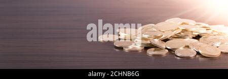 Pièces de monnaie en or dispersées sur une table en bois avec lumière brillante Banque D'Images