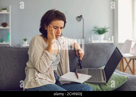 Jeune femme stressée assise près d'un ordinateur portable et touchant le temple avec main Banque D'Images
