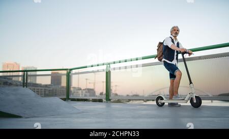 Homme mûr se rendant avec un scooter électrique en plein air en ville, se rendant au travail. Banque D'Images