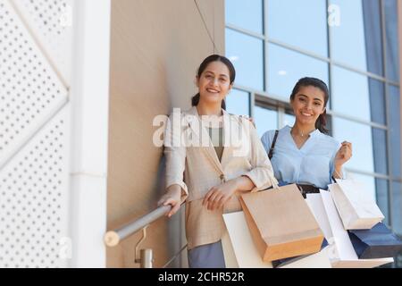 Portrait de deux jeunes femmes tenant des sacs de shopping et souriant à l'appareil photo tout en se tenant à l'extérieur par le centre commercial, l'espace de copie Banque D'Images