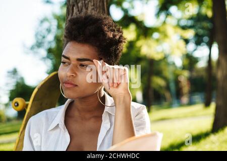 Jeune femme africaine attrayante écrivant dans un journal dans le stationnement Banque D'Images