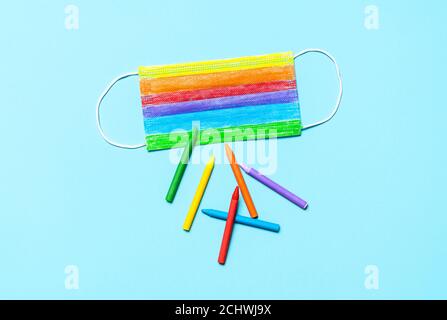 Masque médical coloré en arc-en-ciel et crayons colorés isolés sur un fond bleu sans couture. Vue de dessus du masque de protection multicolore. Retour à l'école ou Banque D'Images
