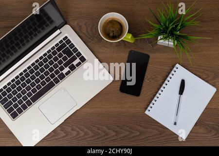 Vue de dessus de l'espace de travail. Table de travail avec ordinateur portable, téléphone portable, café, bloc-notes, stylo et plante avec espace vide fond pour le design. Vue sur la partie plate de dar Banque D'Images