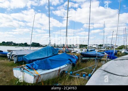 Petits bateaux de voile ou de pêche sur terre avec des mâts et des couvertures sur Mudeford Quay, dans le sud de l'Angleterre, beau ciel bleu ciel nuageux, beaucoup de dingies stockées sur Banque D'Images