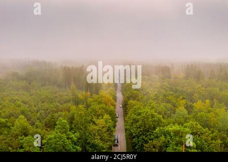 Vue aérienne sur le trafic automobile sur une route entre une forêt dans des conditions brumeuses, belle vue brumeuse de l'oeil d'oiseaux. Banque D'Images