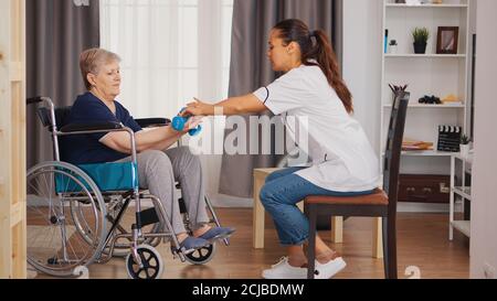 Infirmière aidant une femme âgée en fauteuil roulant avec réadaptation. Formation, sport, récupération et levage, maison de retraite pour personnes âgées, soins infirmiers de santé, soutien de santé, aide sociale, médecin et service à domicile Banque D'Images