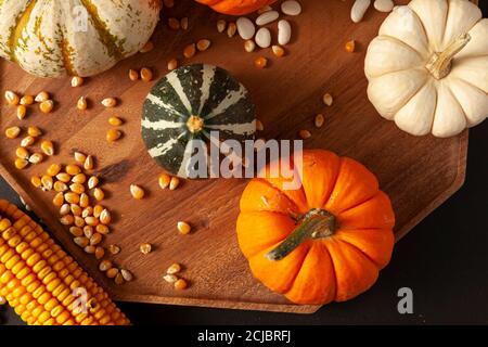 les citrouilles, les cendres et les gourdes, les épis de maïs séchés avec des grains et les haricots secs ont été répartis aléatoirement sur une plaque de bois sur fond noir. Im. Idéale Banque D'Images