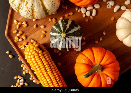 les citrouilles, les cendres et les gourdes, les épis de maïs séchés avec des grains et les haricots secs ont été répartis aléatoirement sur une plaque de bois sur fond noir. Im. Idéale Banque D'Images