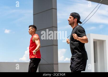 Deux beaux sportifs du Caucase faisant un exercice de corde de saut en plein air le matin sur le toit du bâtiment Banque D'Images