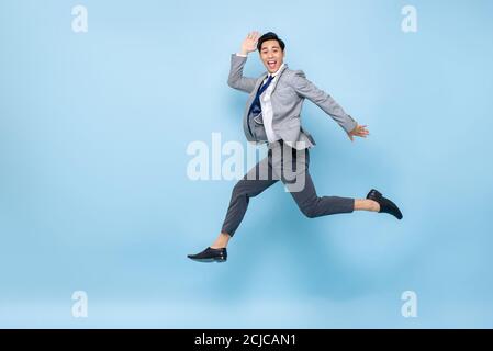 Portrait plein d'amusement plein d'énergie de jeune homme d'affaires asiatique heureux saut en plein air isolé sur fond bleu studio avec copie espace Banque D'Images