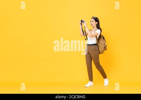 Jeune touriste asiatique prenant des photos avec l'appareil photo isolé arrière-plan jaune Banque D'Images