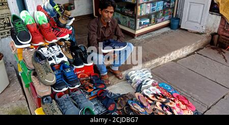 DISTRICT KATNI, INDE - 22 SEPTEMBRE 2019 : un homme asiatique pauvre en ventes montrant des chaussures dans un point de vente de mode à la place du marché de rue de la ville locale. Banque D'Images