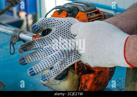 un maître en gants de travail répare le moteur d'un l'ancien coupe-herbe à gaz met des gants Banque D'Images