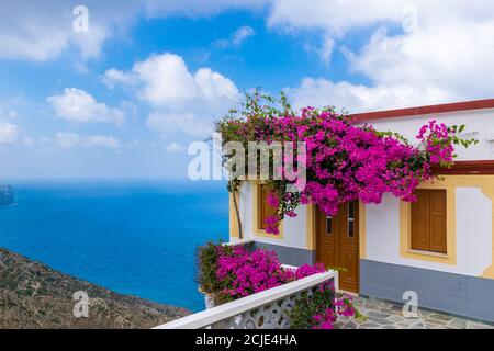 Olympos, Karpathos, Grèce - 16 septembre 2019 : Ageri, maison blanche traditionnelle couverte de fleurs de Bougainvilliers avec mer Égée en arrière-plan Banque D'Images