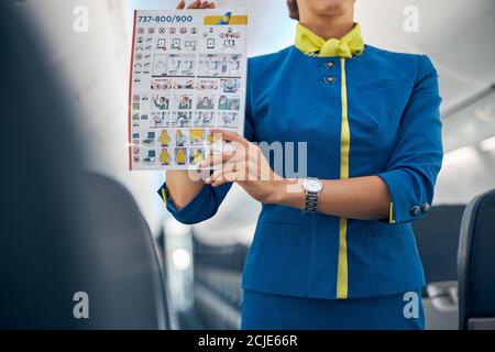 Young attractive air hostess holding safety instructions on a commercial flight in hands Stock Photo