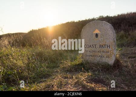 Le soleil se couche sur un marqueur de chemin de pierre South West Coast Path à St Aldhelm Head le long de la côte jurassique près de Swanage, Dorset, Angleterre, Royaume-Uni Banque D'Images