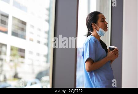 Infirmière surtravaillée dans les exfoliations avec masque prend pause café Dans l'hôpital occupé pendant la pandémie de santé Banque D'Images