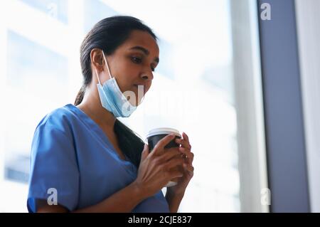 Infirmière surtravaillée dans les exfoliations avec masque prend pause café Dans l'hôpital occupé pendant la pandémie de santé Banque D'Images